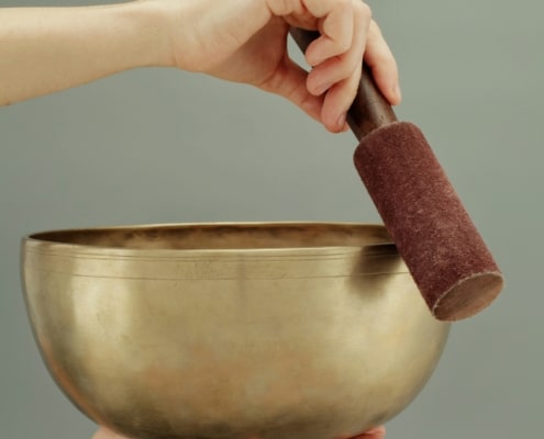 une main qui soutient un bol tibétain et une autre qui le fait chanter en faisant tourner le baton autour